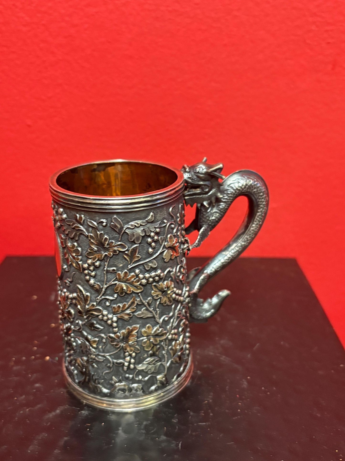 A Chinese export silver mug with flowers and foliage engraved within decorative panels; and a dragon handle. Marked with LC, for Leeching, 利