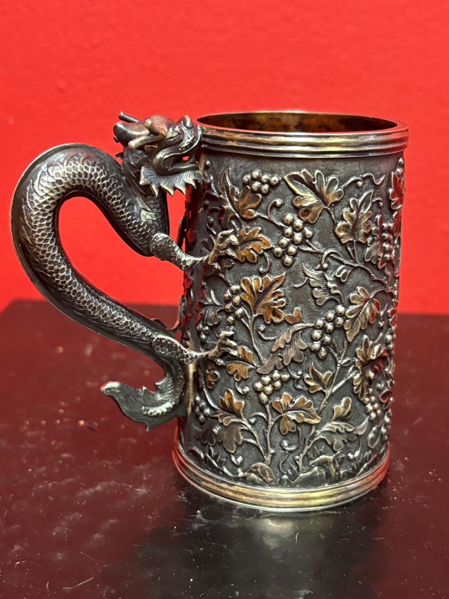 A Chinese export silver mug with flowers and foliage engraved within decorative panels; and a dragon handle. Marked with LC, for Leeching, 利