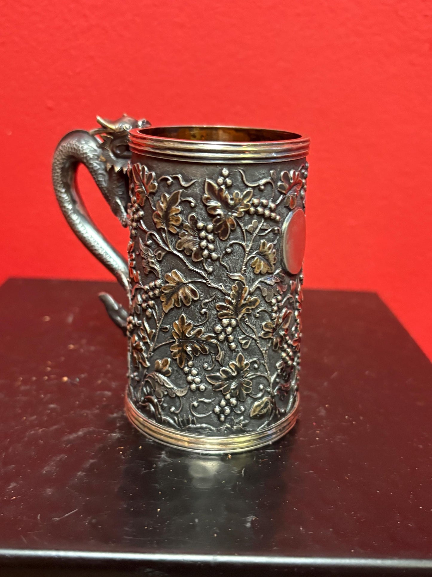 A Chinese export silver mug with flowers and foliage engraved within decorative panels; and a dragon handle. Marked with LC, for Leeching, 利