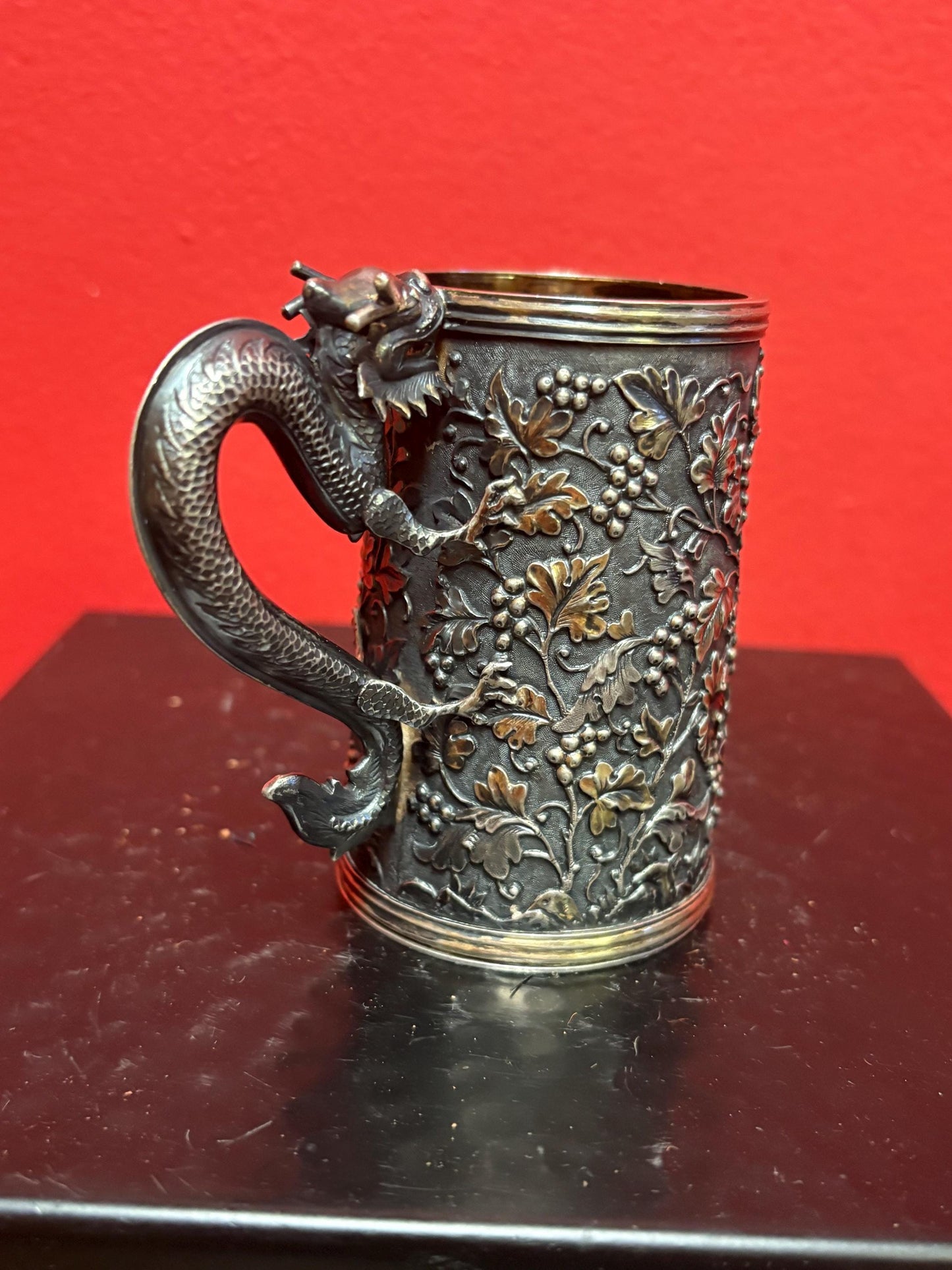 A Chinese export silver mug with flowers and foliage engraved within decorative panels; and a dragon handle. Marked with LC, for Leeching, 利