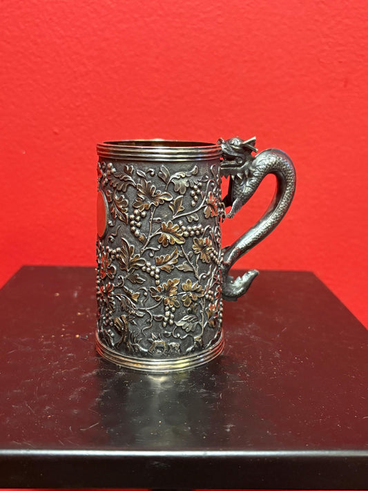 A Chinese export silver mug with flowers and foliage engraved within decorative panels; and a dragon handle. Marked with LC, for Leeching, 利